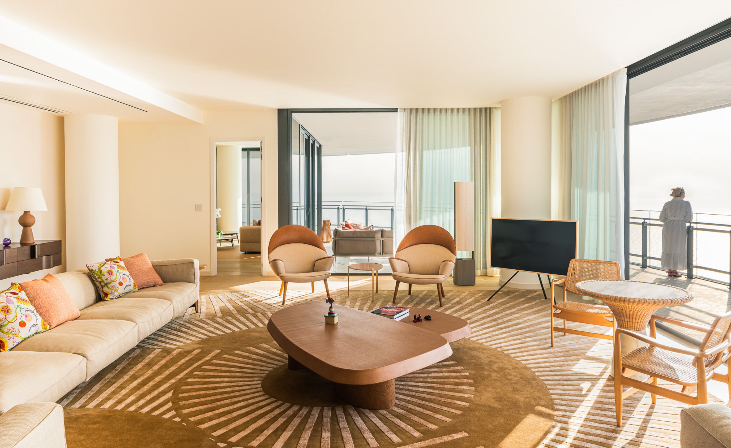 Bright modern living room with floor-to-ceiling windows, neutral-toned furniture, and oceanfront balcony view, featuring a contemporary design with natural light and elegant decor. Build out by Troy Dean Home.