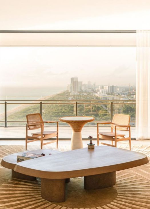 Modern balcony seating area with wooden chairs and a sculptural coffee table overlooking a panoramic city and ocean view. Build out by Troy Dean Home.